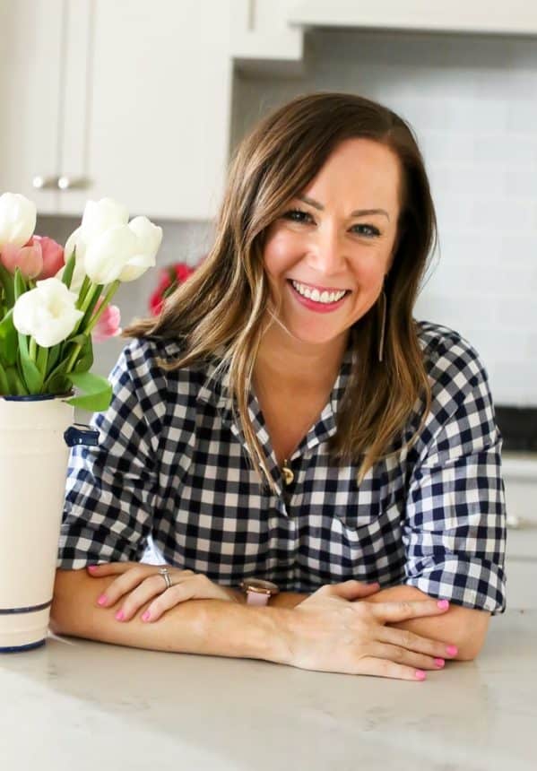 a woman in a plaid shirt is smiling in front of a vase of flowers.
