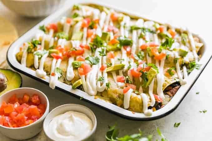 a baking dish filled with healthy chicken enchiladas, set on a table next to bowls of ingredients