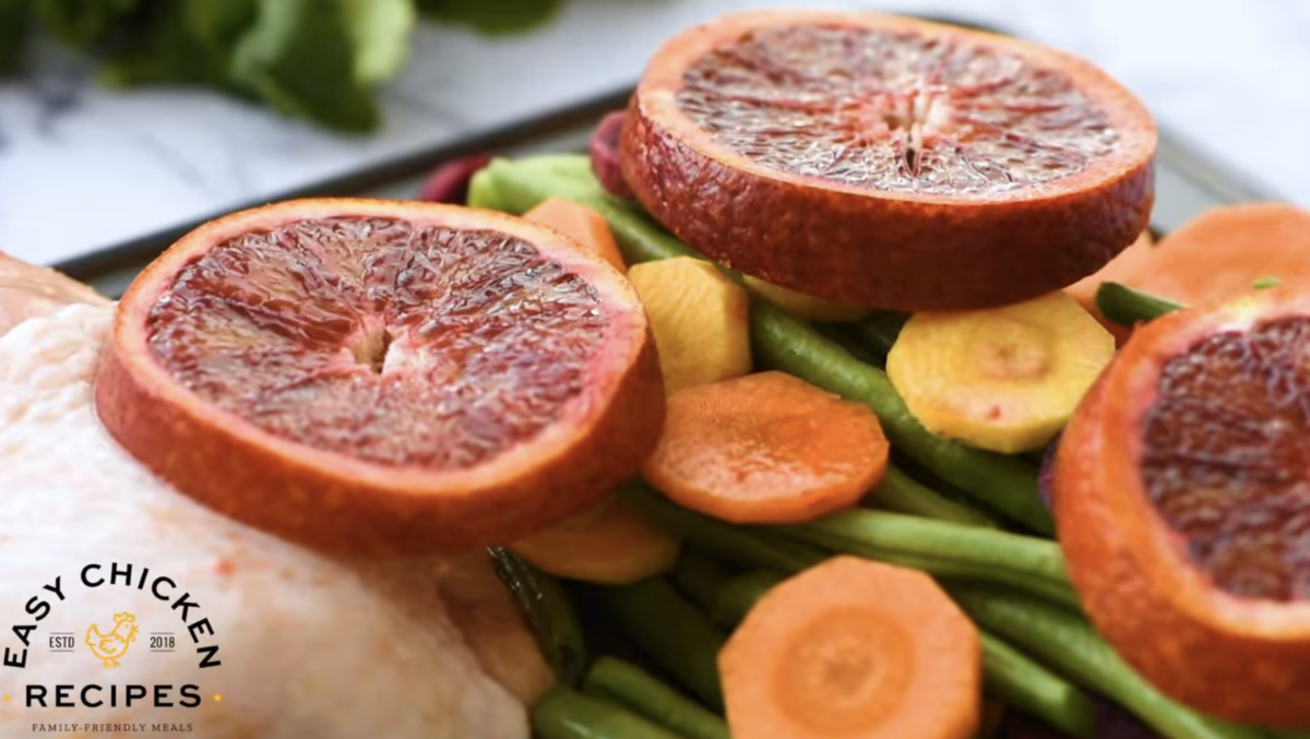Blood orange slices sit atop a baking sheet filled with veggies and chicken thighs. 