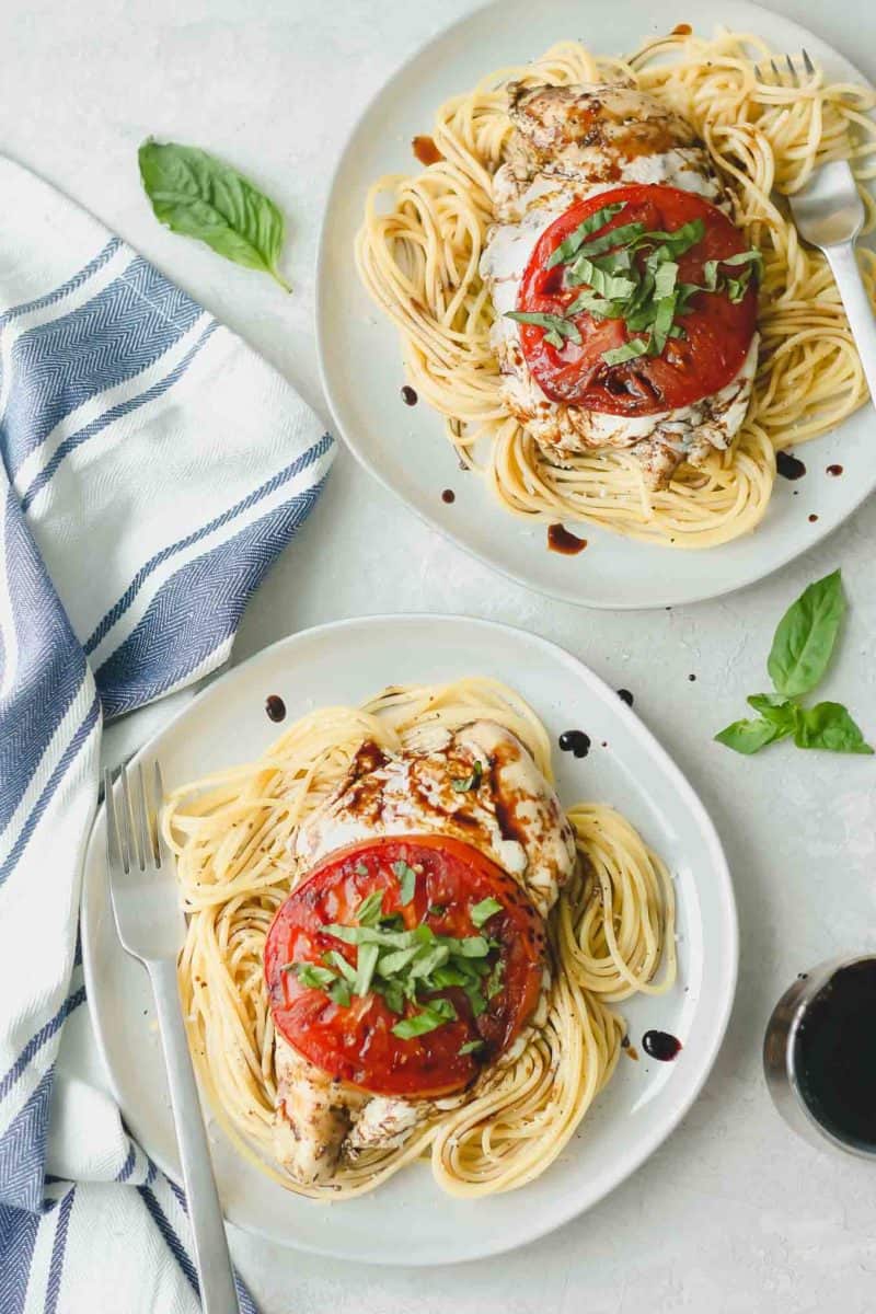 caprese chicken breasts on beds of spaghetti, plated on white dinner plates with forks