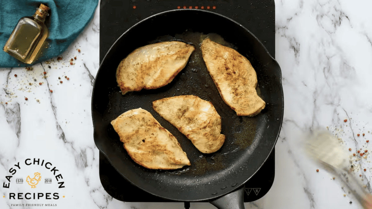 Four seared chicken breasts are in a skillet. 