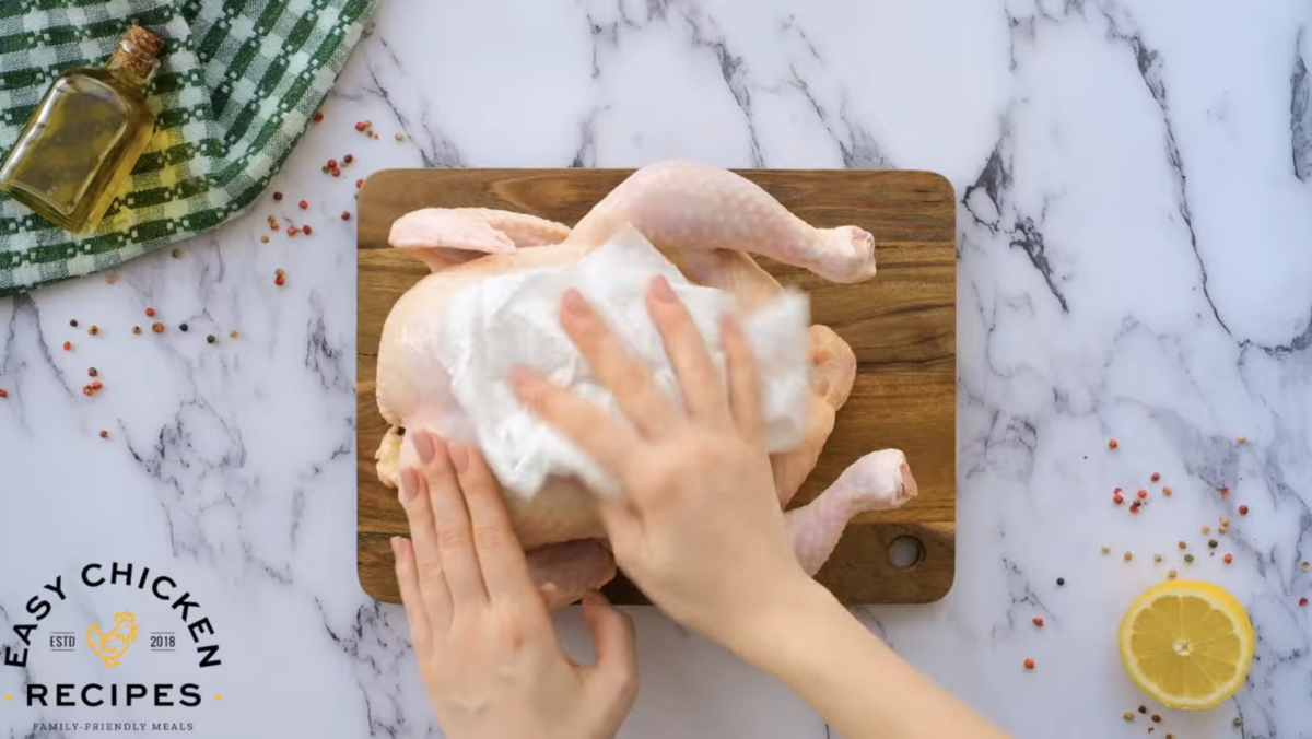 A whole raw chicken is being patted with paper towels.