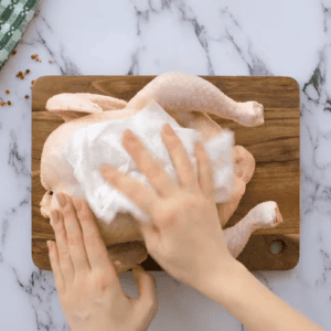 A whole raw chicken is being patted with paper towels.