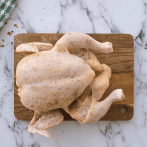 A chicken on a cutting board with lemons and spices.