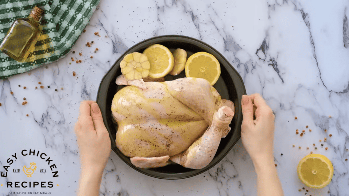 A person holding a chicken in a pan with lemons on it.