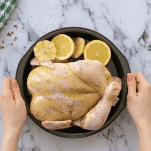 A person holding a chicken in a pan with lemons on it.