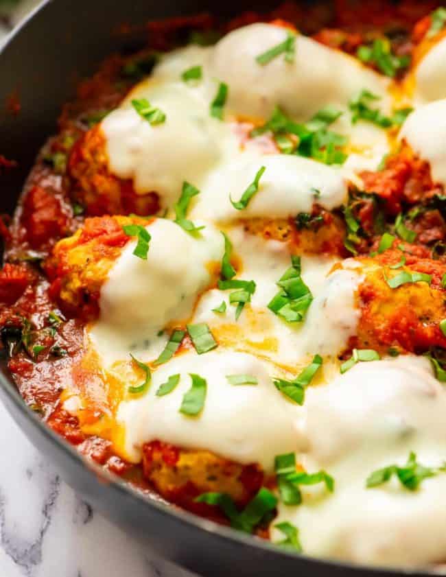 baked chicken meatballs in skillet covered with sauce and cheese