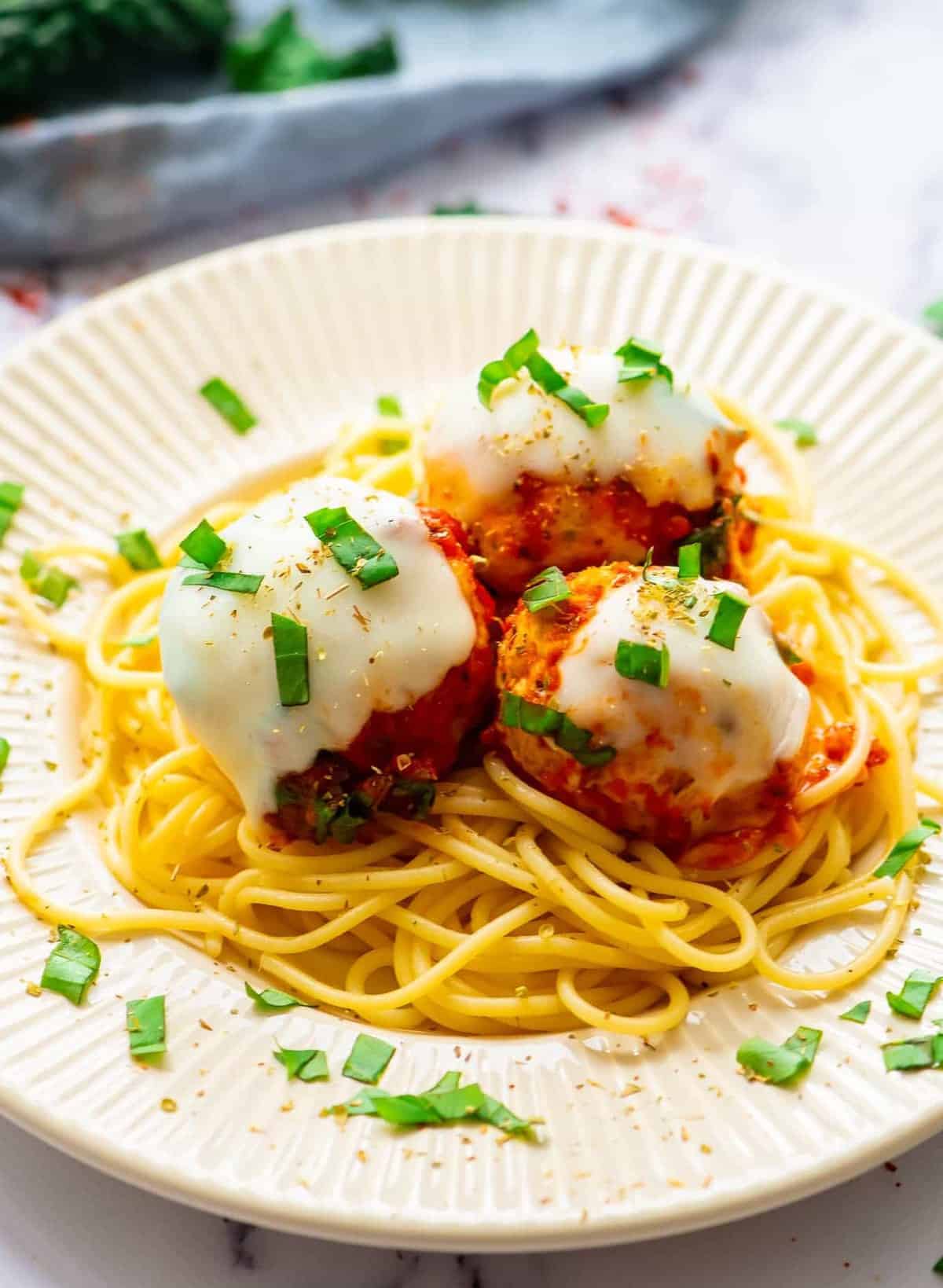 three cheesy chicken meatballs on a plate over pasta