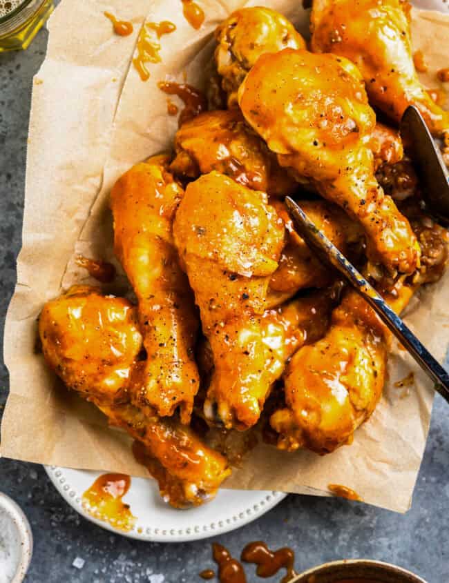 tongs resting on bbq chicken drumsticks on parchment paper.