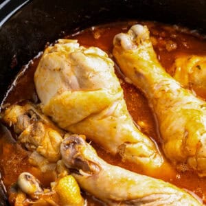 Cooked bone-in, skin-on chicken drumsticks in a crockpot with sauce.