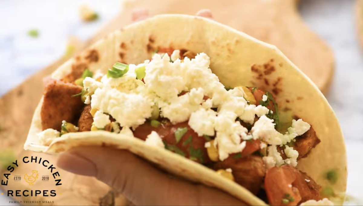 A taco is assembled with chicken, salsa and cheese.