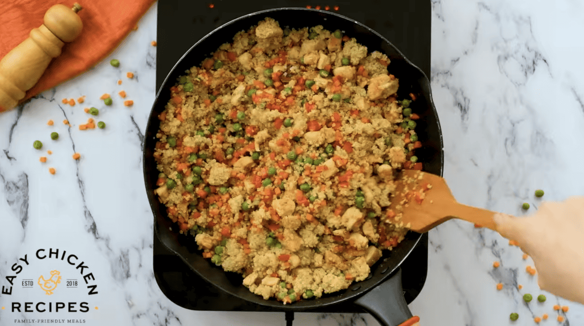 Quinoa fried rice in a skillet with carrots and peas.