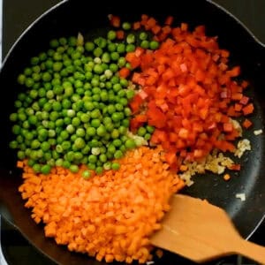 diced carrots, red bell peppers, and peas in a pan with onion.