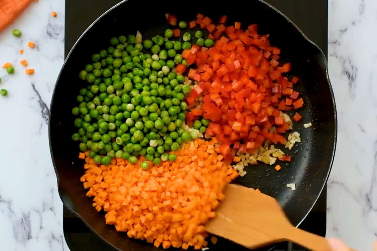 diced carrots, red bell peppers, and peas in a pan with onion.