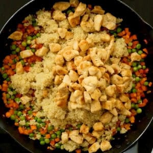 adding cooked quinoa and cooked cubed chicken to a pan with sautéed vegetables.