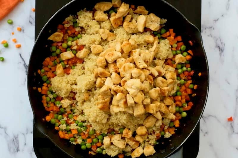adding cooked quinoa and cooked cubed chicken to a pan with sautéed vegetables.