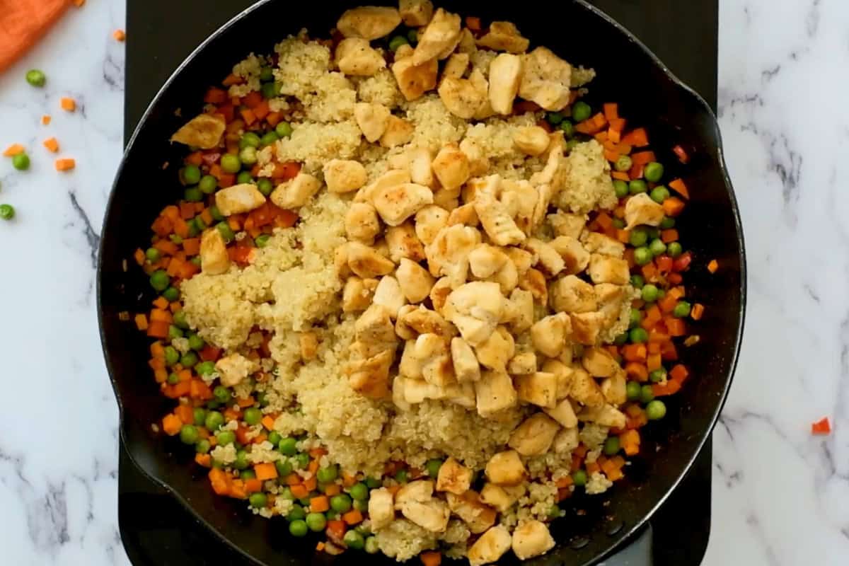 adding cooked quinoa and cooked cubed chicken to a pan with sautéed vegetables.