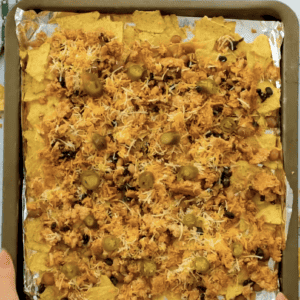 Nachos are spread out on a foil lined sheet pan.