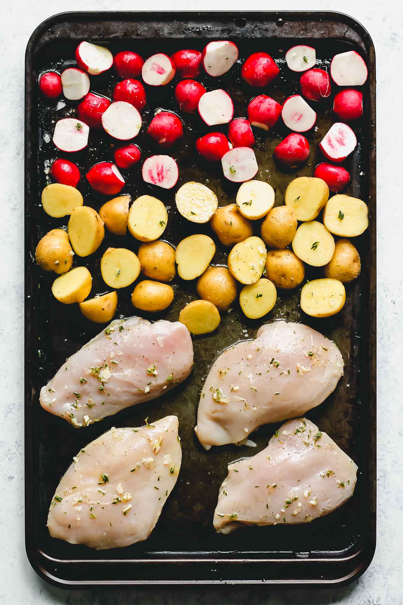 uncooked herb chicken, potatoes and radishes on a sheet pan