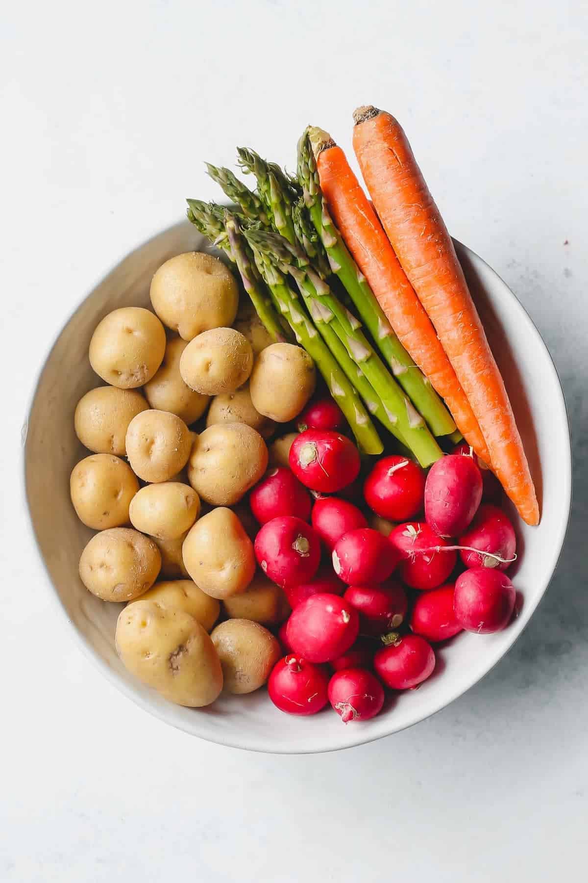 Potatoes, radishes, carrots and asparagus in a bowl