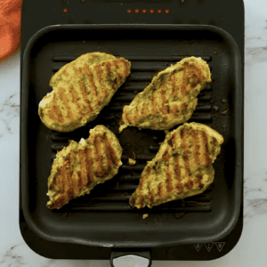 Grilled chicken breasts are on a small griddle.