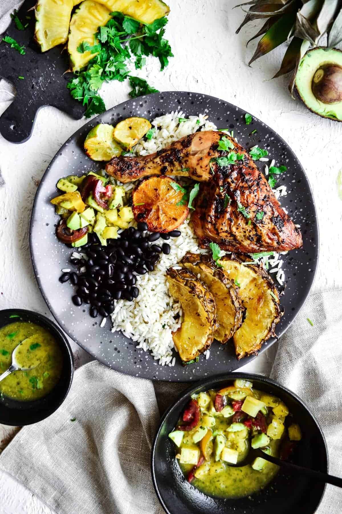 overhead view of cuban chicken on a plate with rice, beans, plantains, and pineapple avocado salsa