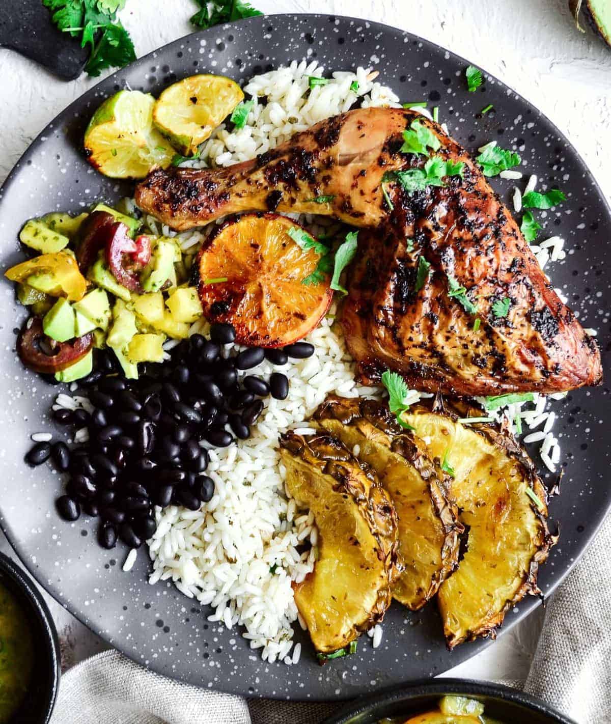 Top shot of Cuban mojo chicken served on a black plate with salsa, rice and black beans