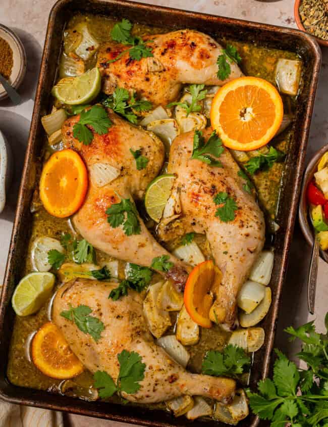 overhead view of cuban mojo chicken on a baking sheet with citrus wedges.