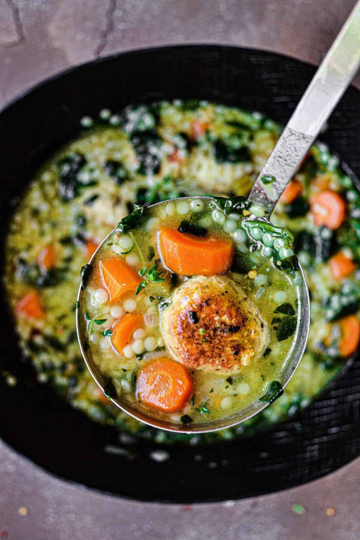 Italian Wedding Soup with chicken meatballs on a spoon held towards camera