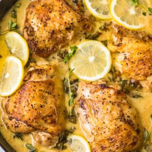 Creamy lemon butter chicken cooked in a skillet with lemons and herbs.