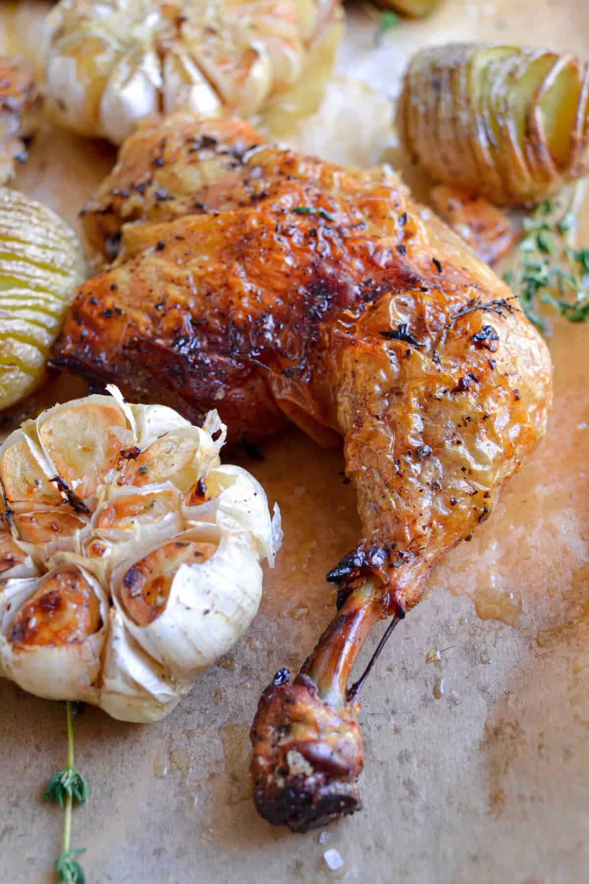 a spatchcock chicken leg next to roasted garlic