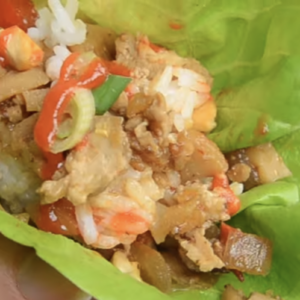 A chicken lettuce wrap is garnished with cashews, green onions and sriracha.