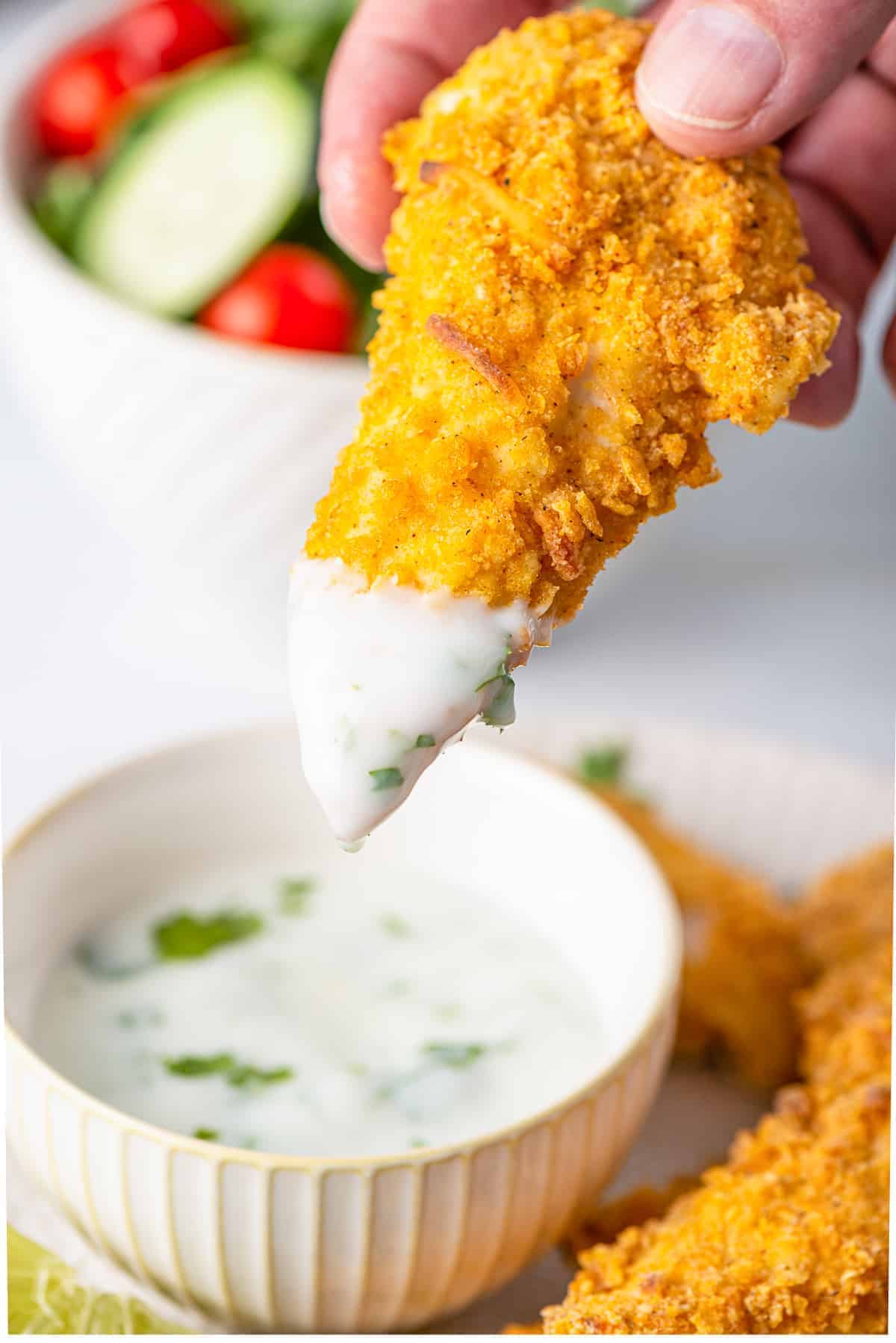 Dipping a breaded chicken finger into a yogurt sauce.