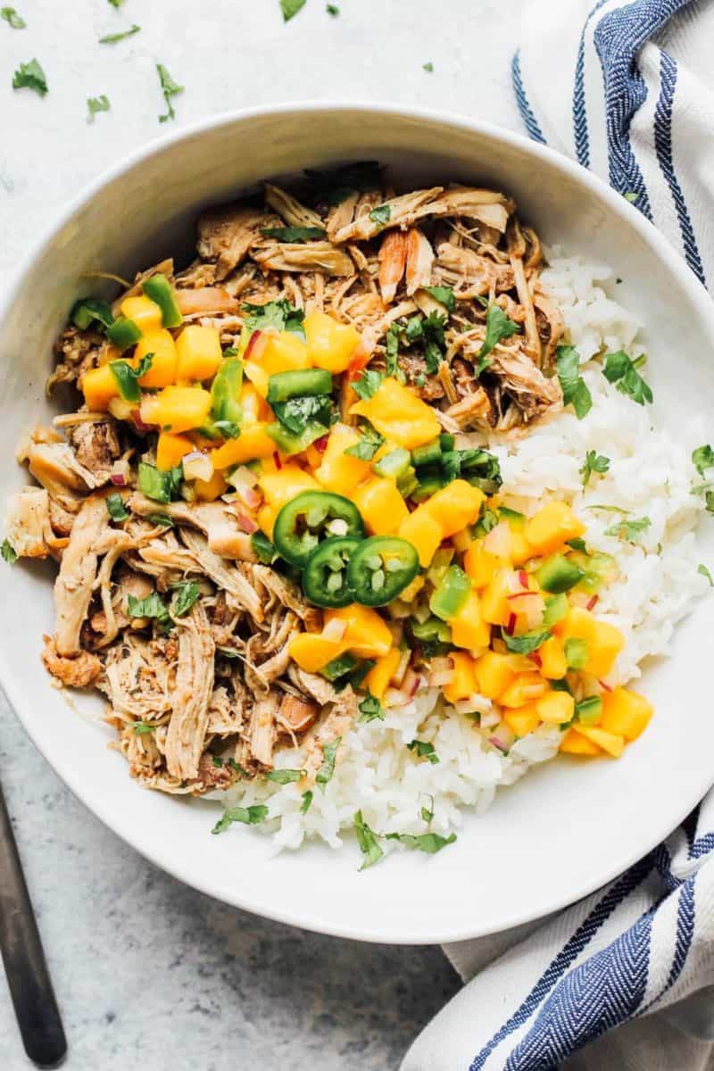A white bowl with Instant Pot Jerk Chicken and mangoes on it.