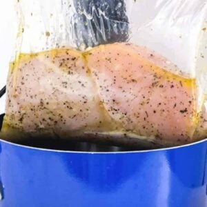 A person holds sous vide chicken breast in a blue pot.