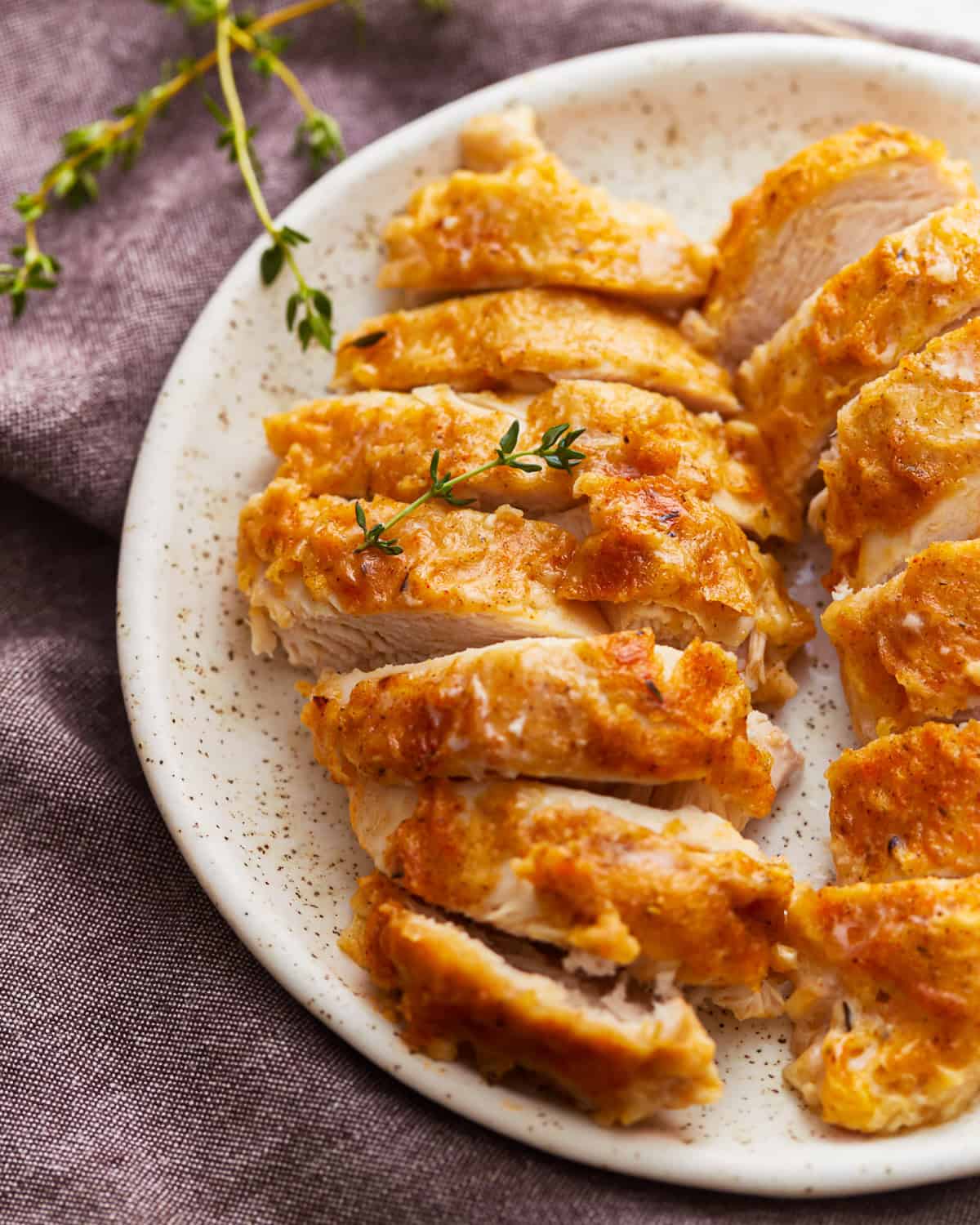 sliced butter baked chicken breasts on a white plate.