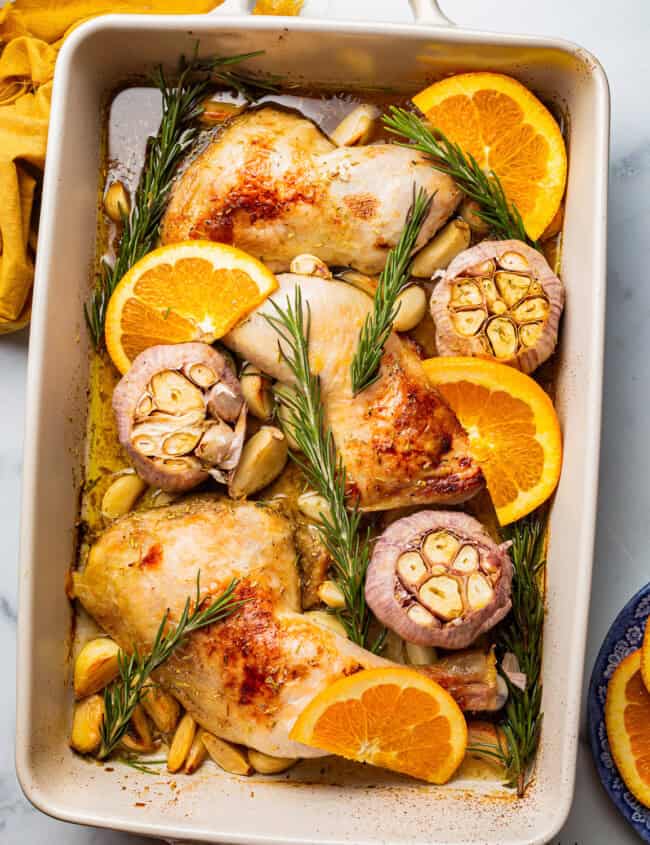 overhead view of chicken with 40 cloves of garlic in a baking dish.