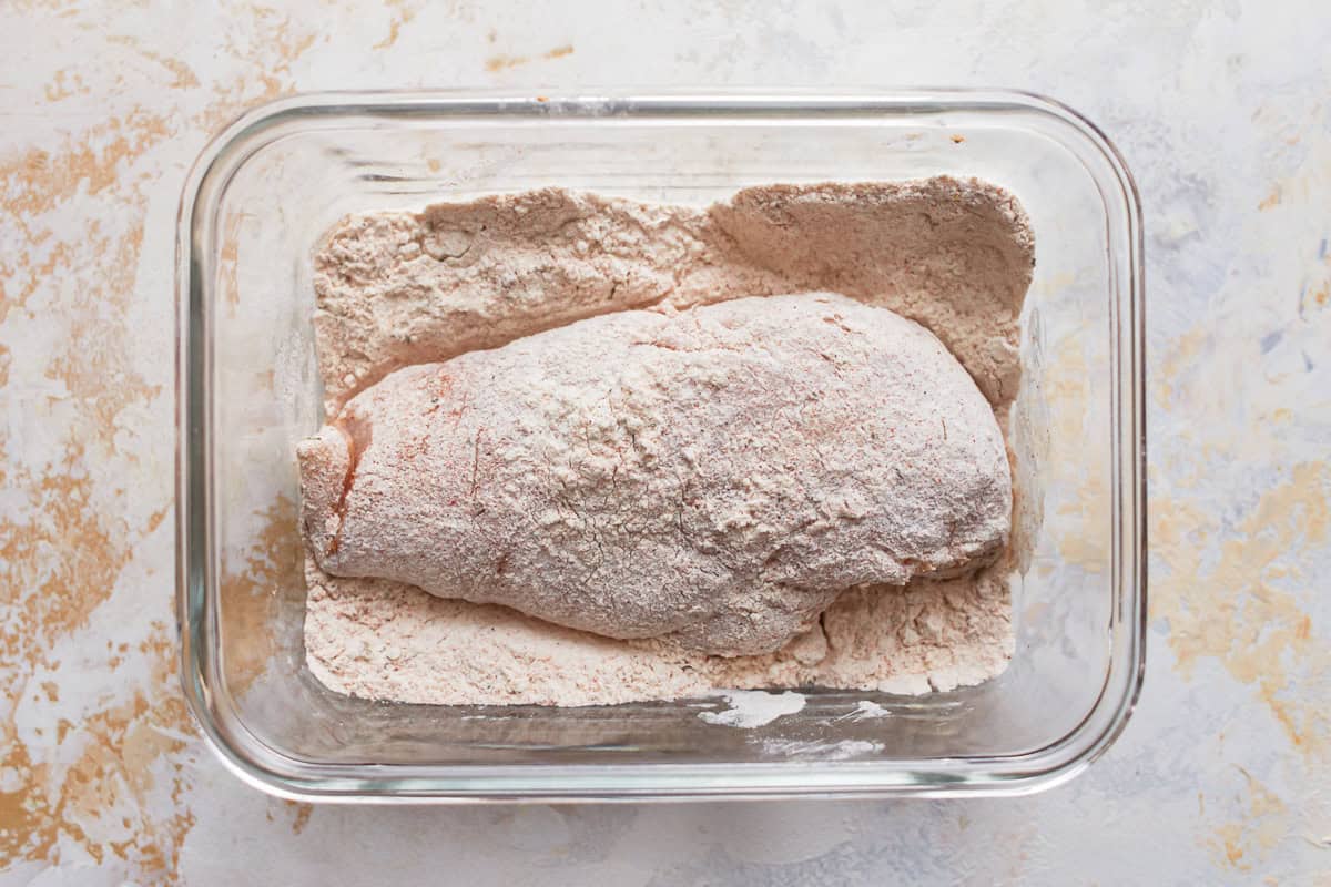 a chicken breast dredged in flour in a glass dish.