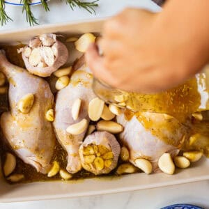 pouring marinade over chicken and garlic in a baking dish.