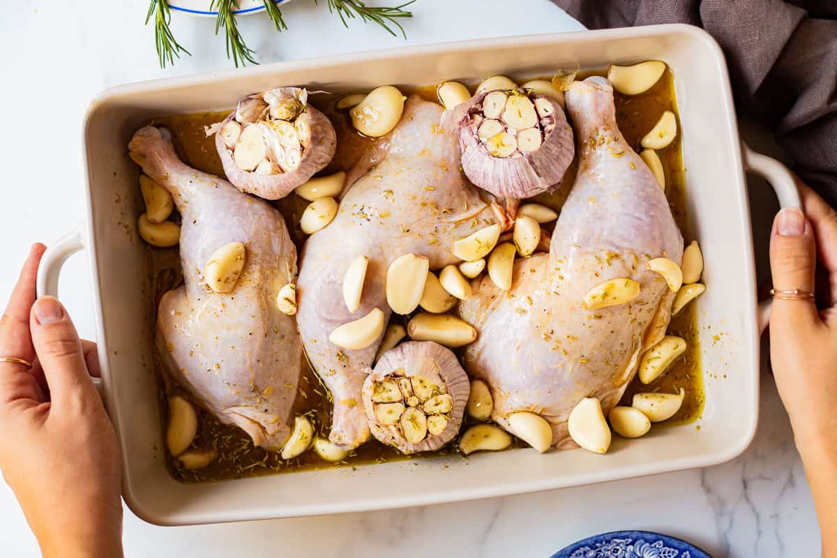 unbaked chicken with 40 cloves of garlic in a baking dish.
