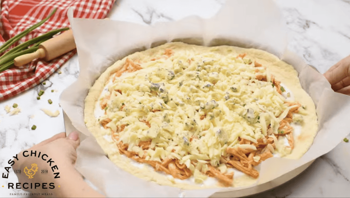 A person is putting buffalo chicken on top of a pizza.