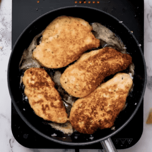 Chicken breasts are cooking in a pan.
