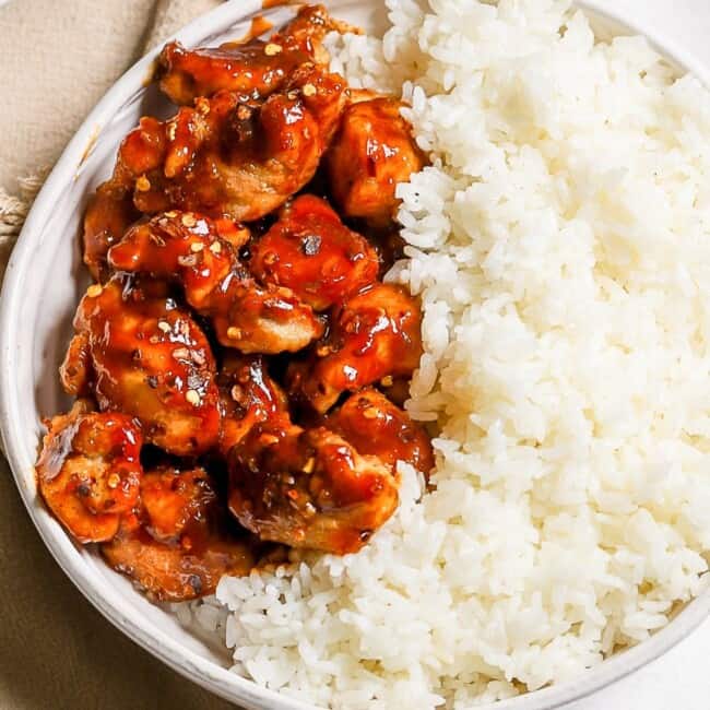 A bowl of rice with General Tso's chicken and sauce on it.