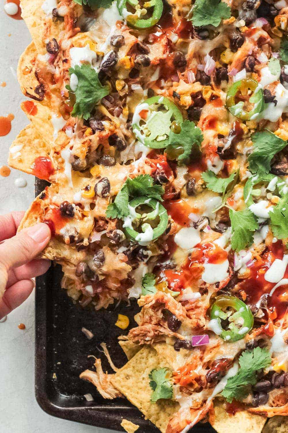 A hand pulling out a tortilla in the BBQ Chicken Nachos