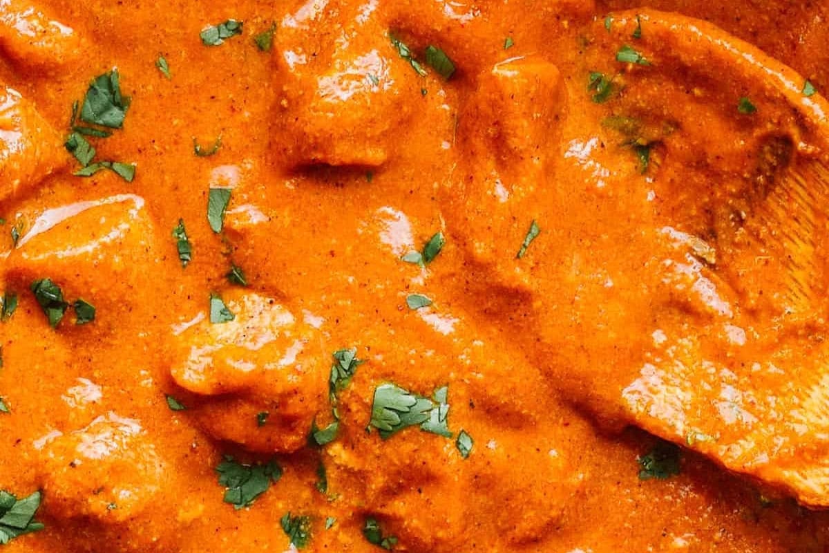 closeup of butter chicken in a pan with a wooden spoon.