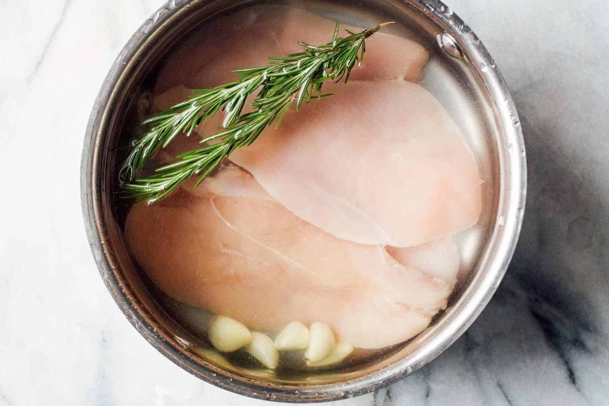 how to poach chicken - chicken in a pot with rosemary and garlic cloves.