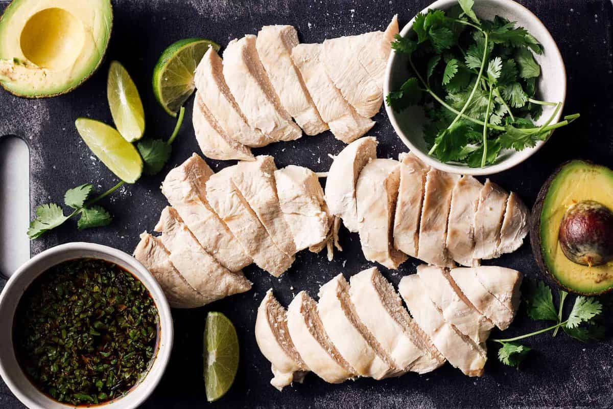 sliced poached chicken on plate with sauce and cilantro.