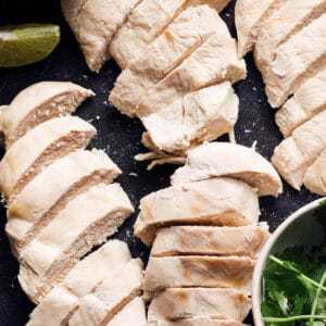 overhead view of sliced poached chicken breasts on a cutting board.