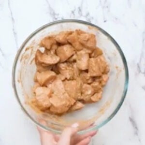 marinating chicken pieces in seasoned yogurt in a glass bowl.