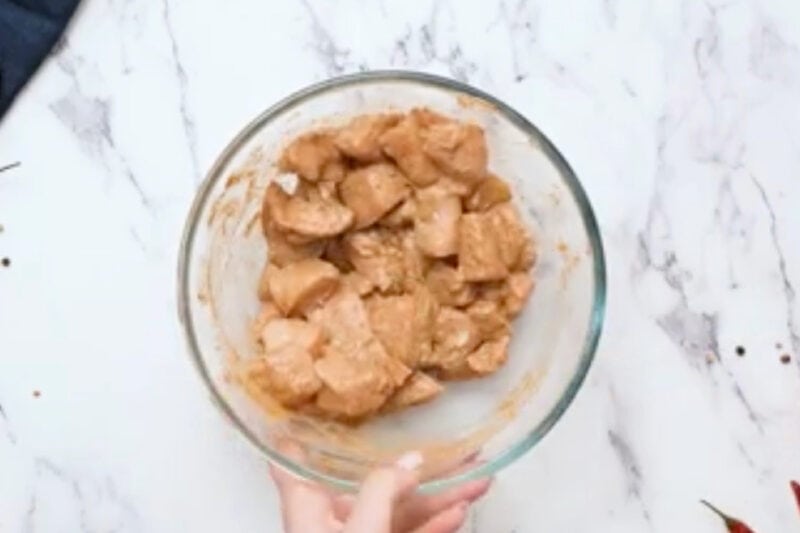 marinating chicken pieces in seasoned yogurt in a glass bowl.